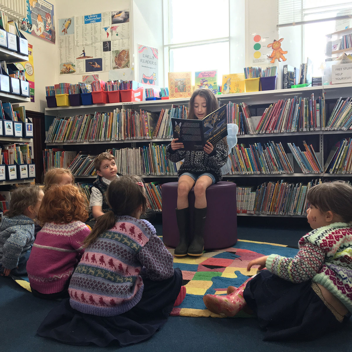 Child reading a book out loud to a group of her peers